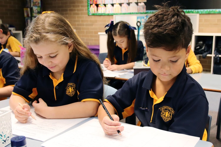 2 Stage 1 students writing in the their exercise books in the classroom