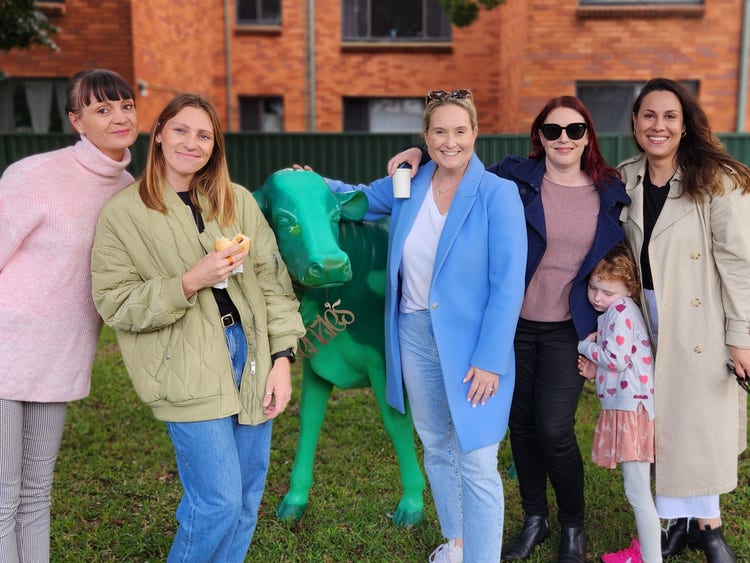 A group of mums stood beside a green cow at the mother's day breakfast