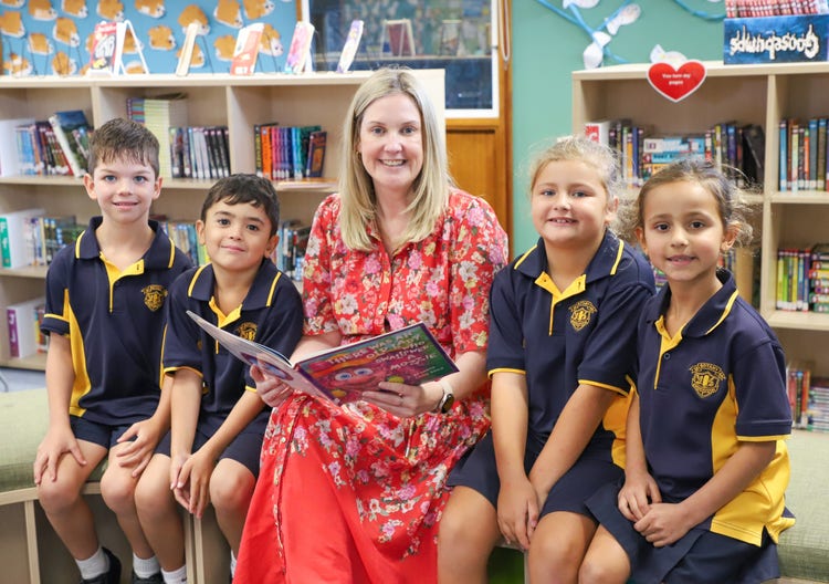 Principal reading a book with 4 students in the school library
