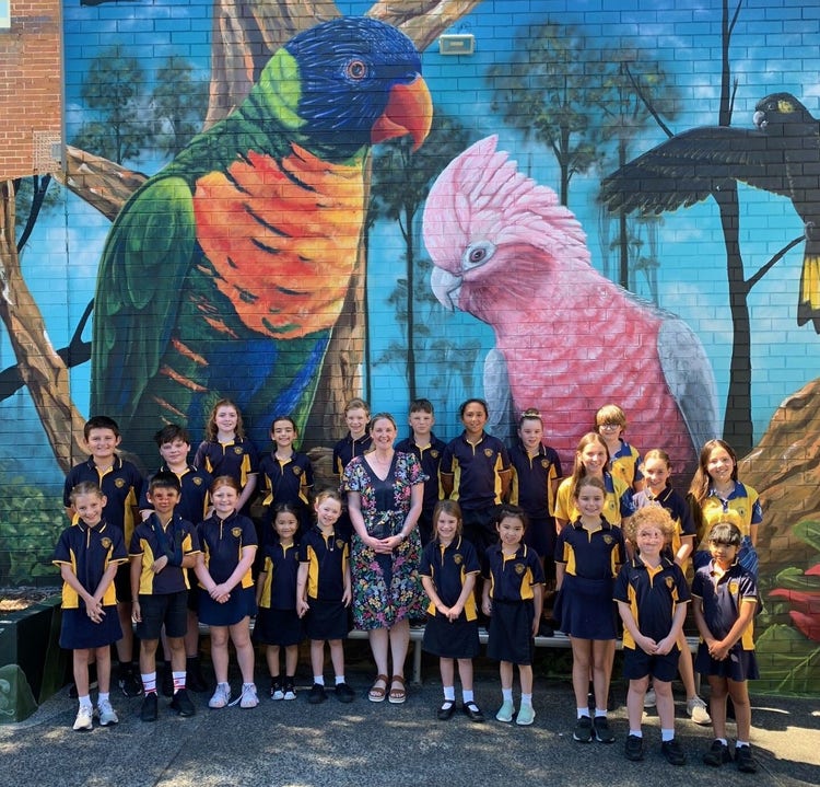 The principal standing with a group of students in front of the school mural