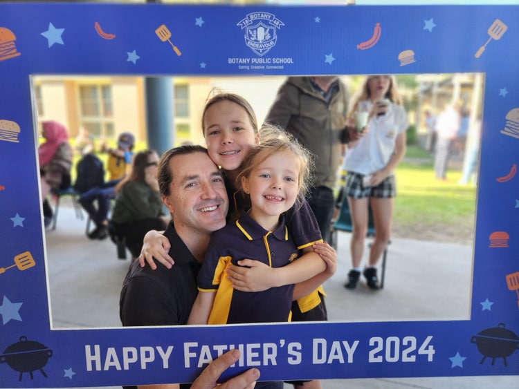 a dad with his 2 daughters, posing in a father's day banner