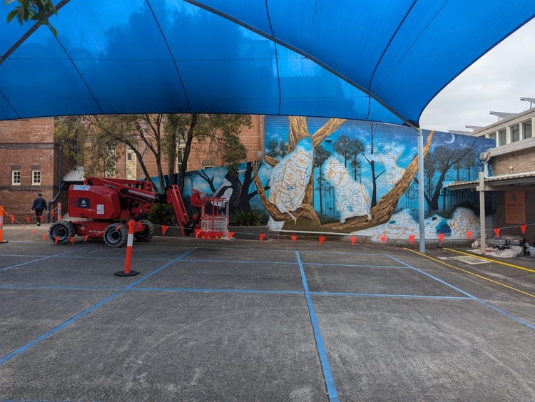 a cherry picker in front of a hlaf-completed school mural in the courtyard