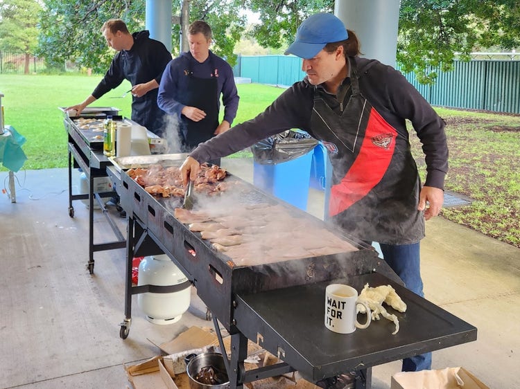 3 parents cooking bacon at a school bbq
